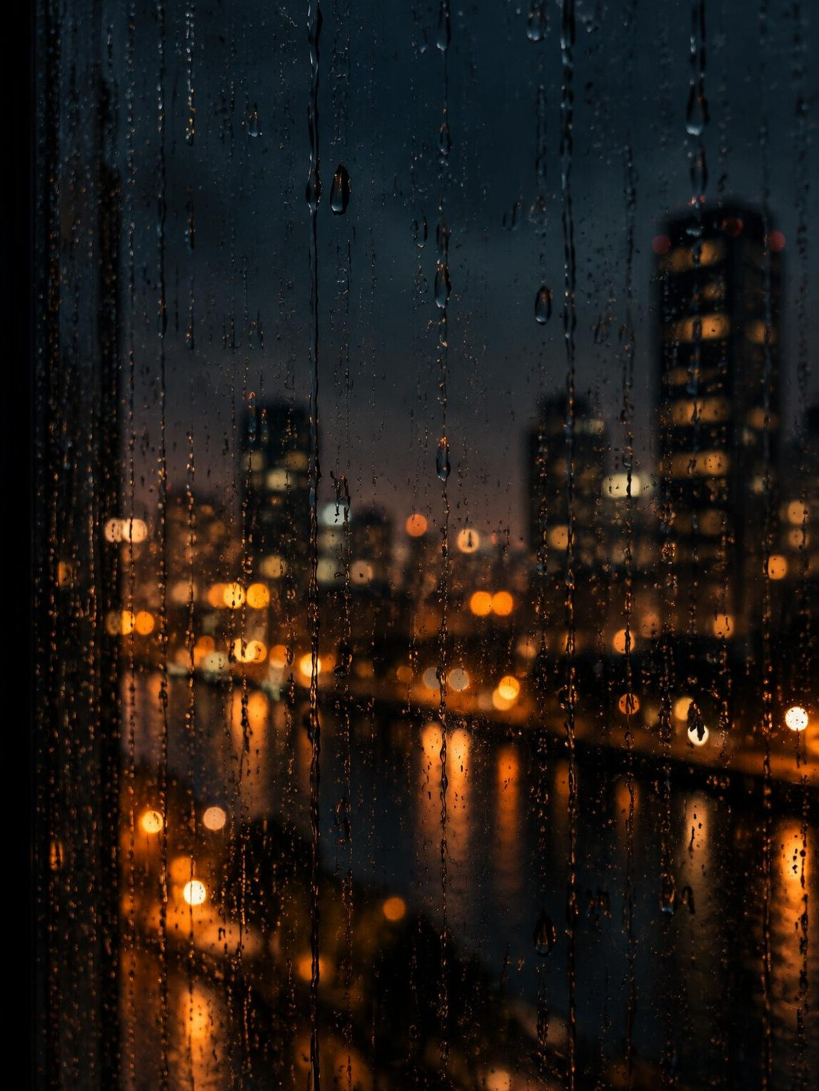 Raindrops on a dark window with blurred city lights